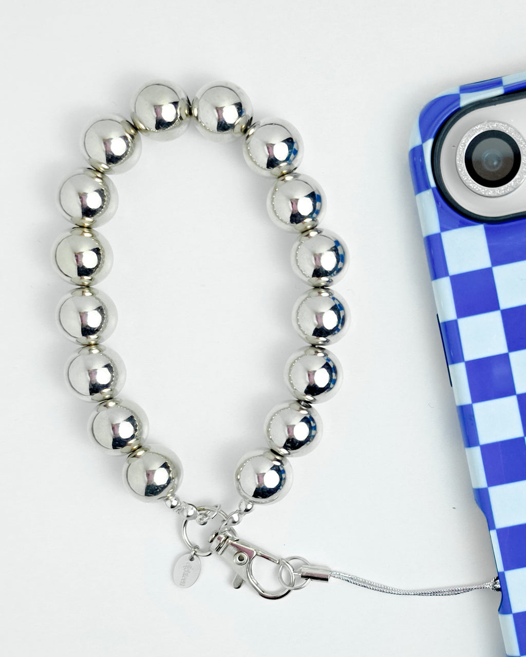 A silver beaded phone strap with a clasp and cord, shown next to a blue and white checkered phone case on a white background.