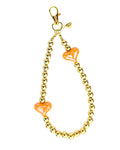 A gold-tone beaded chain accessory with two translucent orange heart-shaped beads, featuring a lobster clasp at the top, shown on a plain white background.