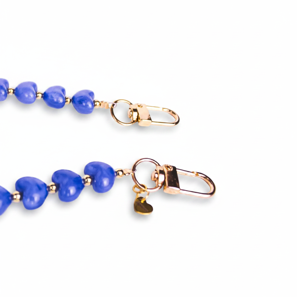 A honeysuckle blue, heart shaped phone charm with gold lobster clasp closures and gold spacer beads in between each heart. A gold branded heart shaped tag is attached to the closure on the right