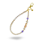 A gold and fine crystal phone charm with amber and lavender beaded accents. Round, white beads spell out "BLESSED" in gold letters on the charm. Accented with a heart shaped brand tag attached to the golden lobster claw clasp