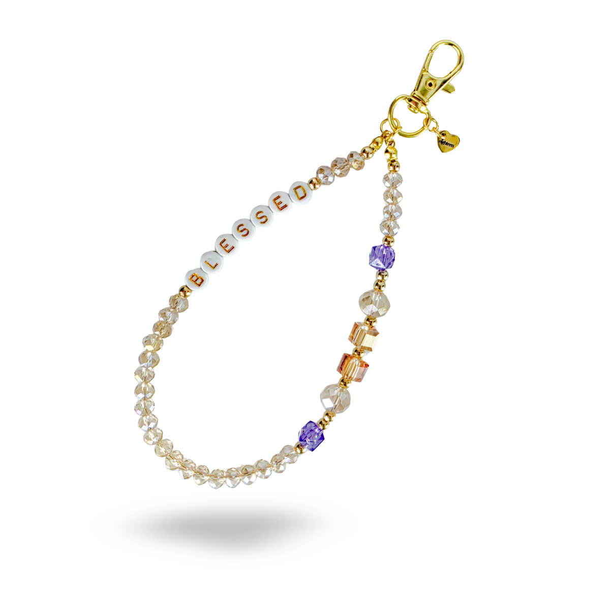 A gold and fine crystal phone charm with amber and lavender beaded accents. Round, white beads spell out "BLESSED" in gold letters on the charm. Accented with a heart shaped brand tag attached to the golden lobster claw clasp