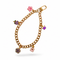 A gold-tone curb link chain Phone charm featuring colorful enamel charms, including a pink flower, a purple rose, a pink book, and a dark blue gemstone ball, displayed on a clean white background.