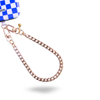 A rose gold metal chain strap with a lobster clasp, shown attached to a blue and white checkered bag corner on a plain white background.