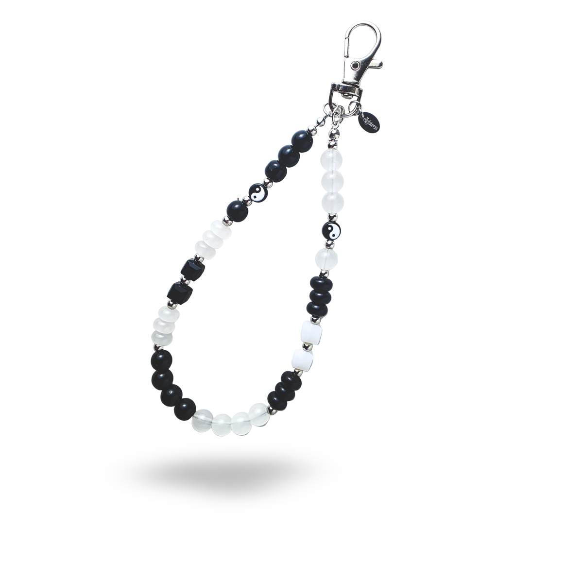 A black and white beaded Yin and Yang phone charm with an oval logo tag attached on the silver lobster claw clasp